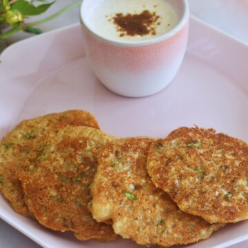 Farali Rajgira and Sabudana Thalipeeth served in a pink plate with some yogurt served too and some flowers in the background.