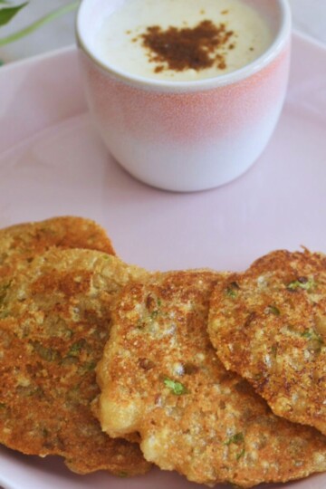 Farali Rajgira and Sabudana Thalipeeth served in a pink plate with some yogurt served too and some flowers in the background.