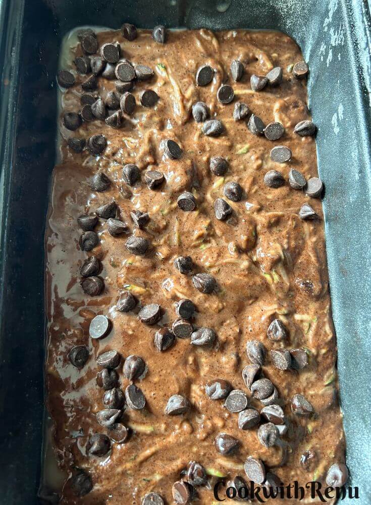 Zucchini Cake ready to be baked with chocolate chips on it in a loaf tin.