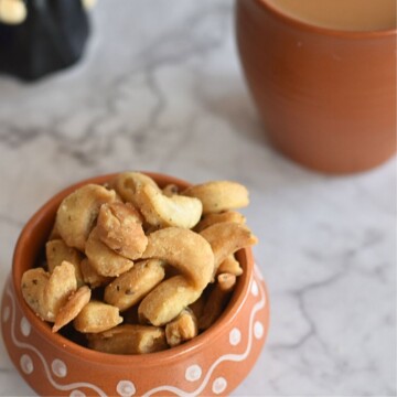 Close up view of Namkeen Kaju Matri or Namak Para served in a brown designer bowl with a cup of tea and teapot seen in the background.