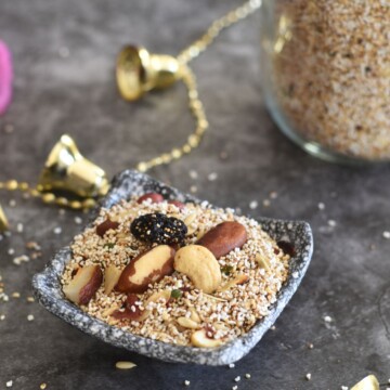 Amaranth Trail mix served in a small black plate. Seen in the background is some golden bells and a jar filled with rajgira.