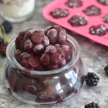 Frozen blackberries in a glass jar and in a Ice-Tray, with some black berries in the background.