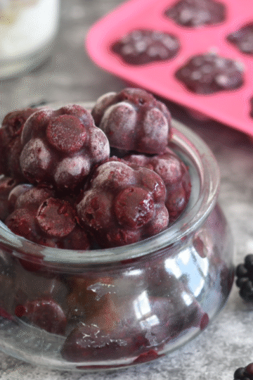 Frozen blackberries in a glass jar and in a Ice-Tray, with some black berries in the background.