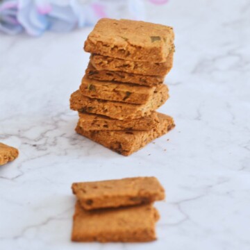 Keto Cheese and Chive Crackers stacked on a white paper, with some artificial flowers in the background.