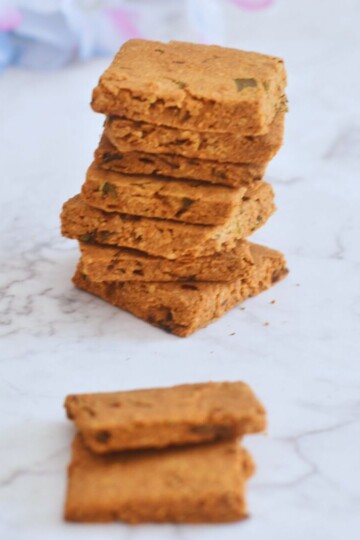 Keto Cheese and Chive Crackers stacked on a white paper, with some artificial flowers in the background.