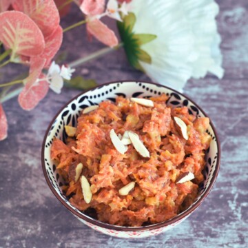 No ghee no mawa gajar halwa served in a designer white and black bowl with some artificial flowers in background.