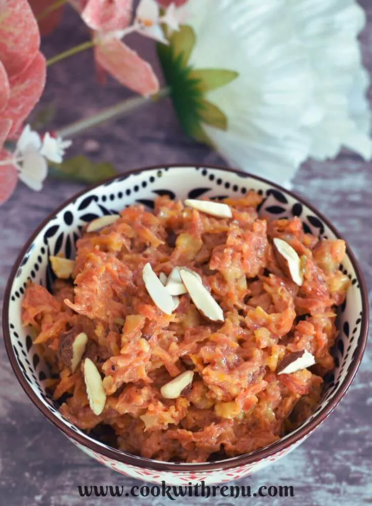No ghee no mawa gajar halwa served in a designer white and black bowl with some artificial flowers in background.