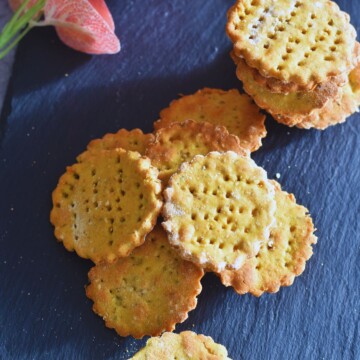 Baked Chickpea Crackers scattered on a black cheese baord.