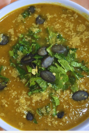 Top view of Soup served in a white bowl with a topping of seeds and celery leaves.
