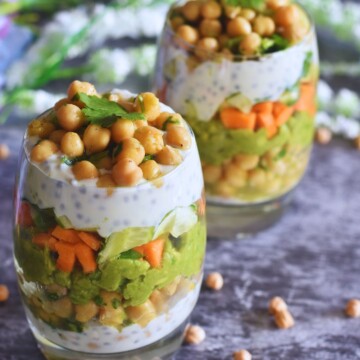 Chickpeas Avocado Lunch Parfait served in 2 glasses. Seen in the background are some chickpeas and some flowers.