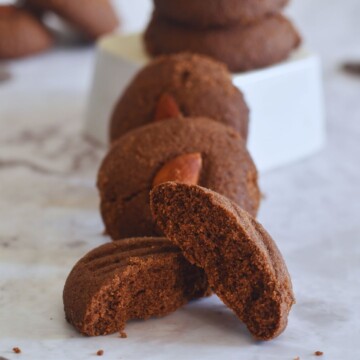 Few Whole Wheat Chocolate Nankhatai arrranged on a white sheet. In the front is one half of nankhatai showing the texture of inside.