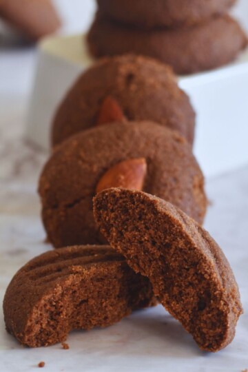 Few Whole Wheat Chocolate Nankhatai arrranged on a white sheet. In the front is one half of nankhatai showing the texture of inside.