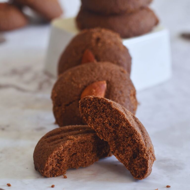 Few Whole Wheat Chocolate Nankhatai arrranged on a white sheet. In the front is one half of nankhatai showing the texture of inside.