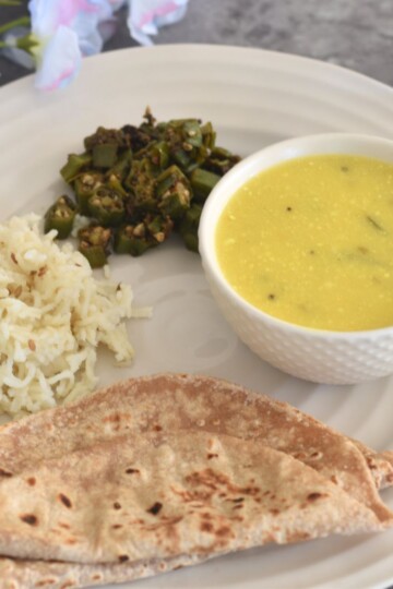 Lunch thali served which has khapli wheat roti, jeera rice, bhindi and takhachi kadhi.