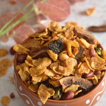 Leftover Cornflakes Chivda served in a designer bowl. Seen in the background are some artificial flowers.