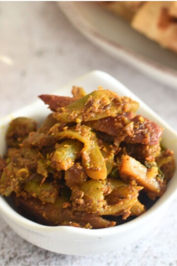 Aloo Parwal served in a white bowl. Seen in the background are some roti in a plate.
