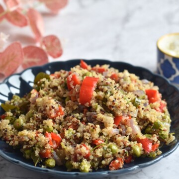 Quinoa Pulav served in a blue plate. seen in the backgroud in a bowl of yogurt and some artifical flowers.