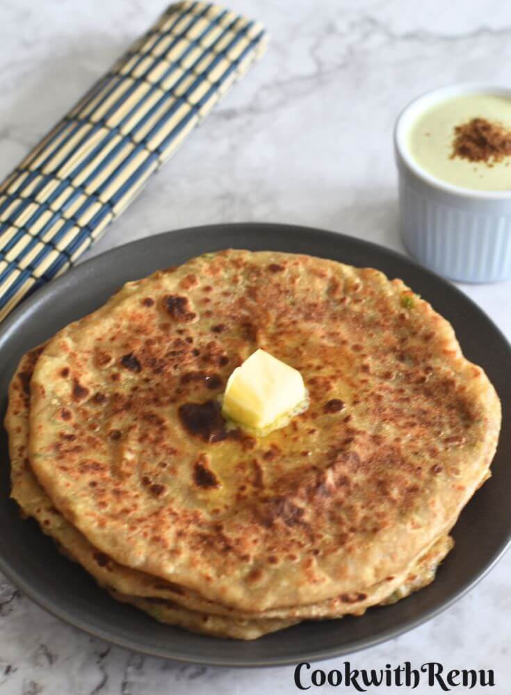 Aloo Paratha in a grey plate, with a dollop of butter and some pudina raita in a bowl.