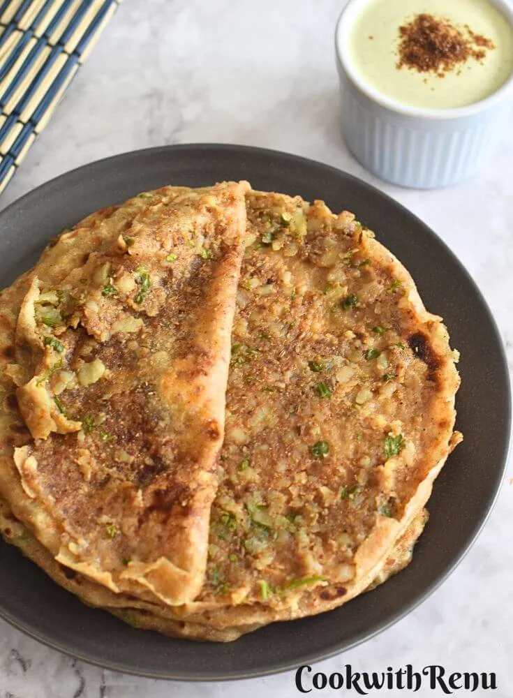 Pic showing Inner texture of Aloo Paratha served on a grey plate with some pudina raita in a bowl.