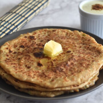 Aloo Paratha in a grey plate, with a dollop of butter. and pudina raita in a bowl.