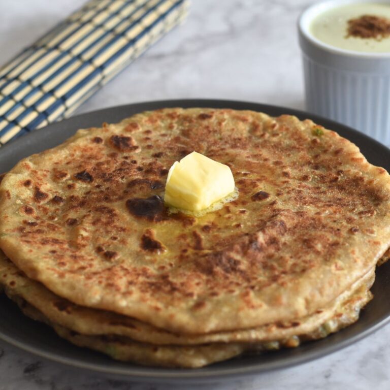 Aloo Paratha in a grey plate, with a dollop of butter. and pudina raita in a bowl.