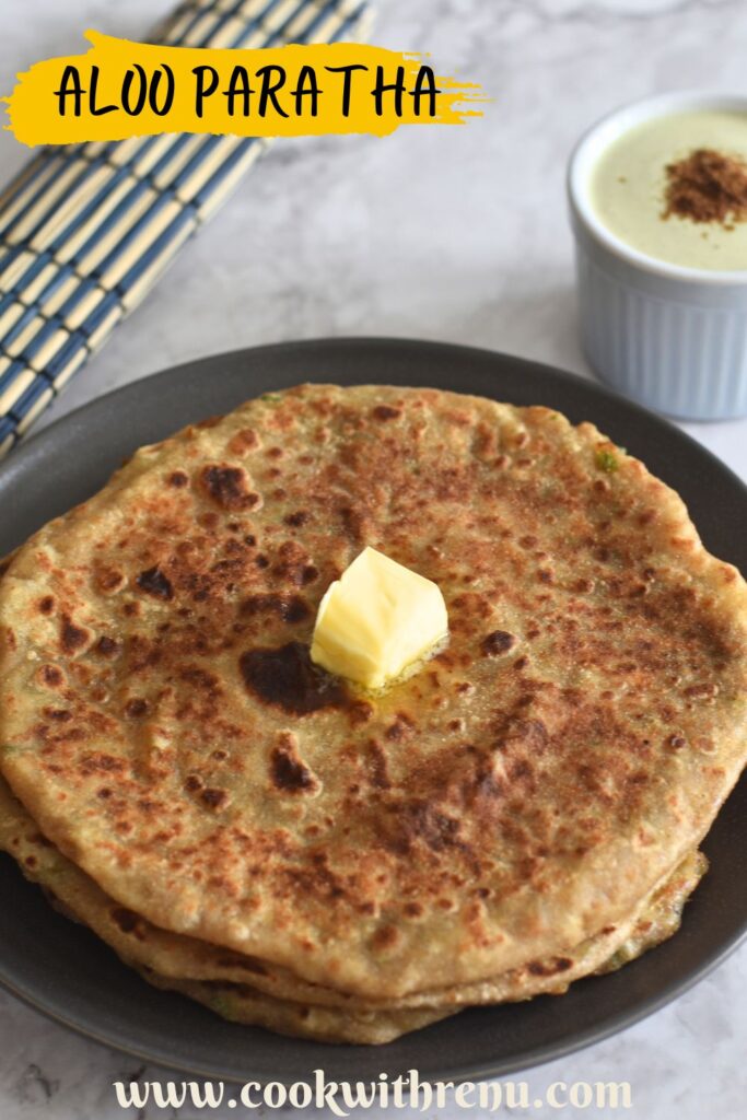 Aloo Paratha in a grey plate, with a dollop of butter. and pudina raita in a bowl.