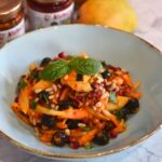 Sweet and Spicy Mango Salad served in a light blue bowl with some mangoes and sauce in the background.