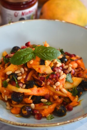 Sweet and Spicy Mango Salad served in a light blue bowl with some mangoes and sauce in the background.