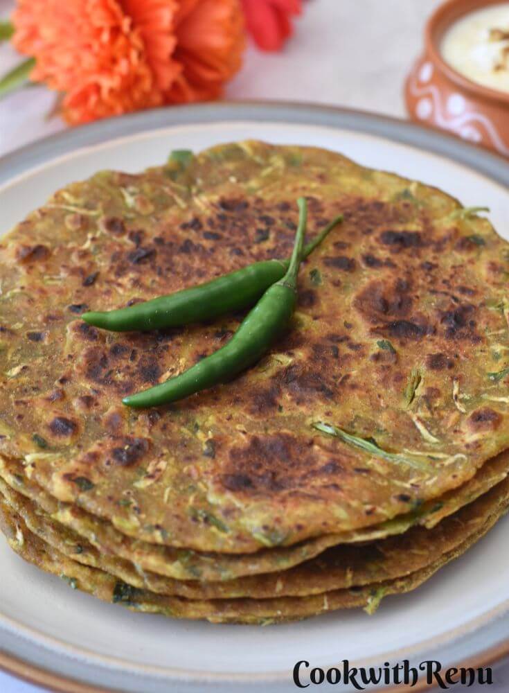 3-4 Dudhi Paratha served in a white plate with some green chilies on top and some yogurt in a bowl.