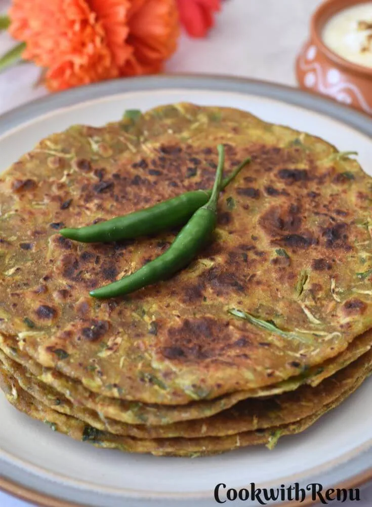 3-4 Dudhi Paratha served in a white plate with some green chilies on top and some yogurt in a bowl.