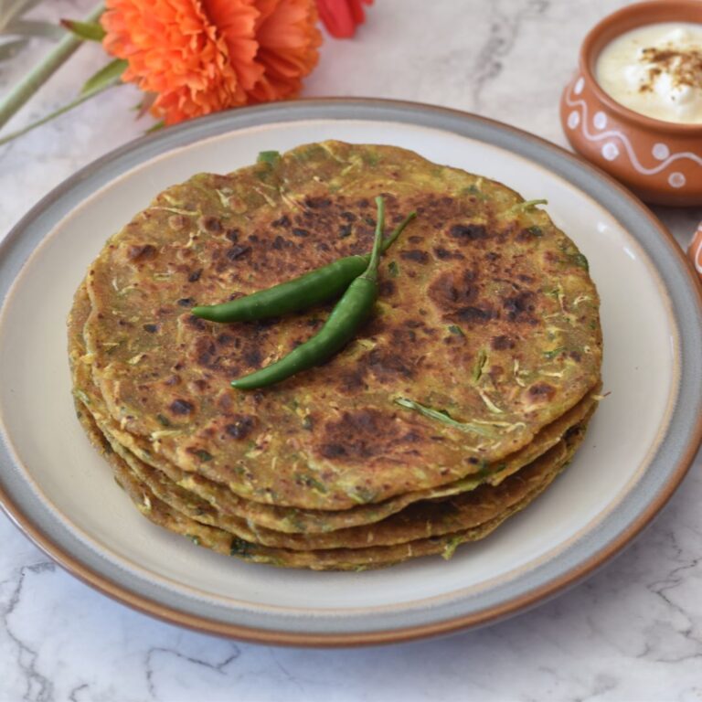 3-4 Dudhi Paratha served in a white plate with some green chilies on top and some yogurt in a bowl.