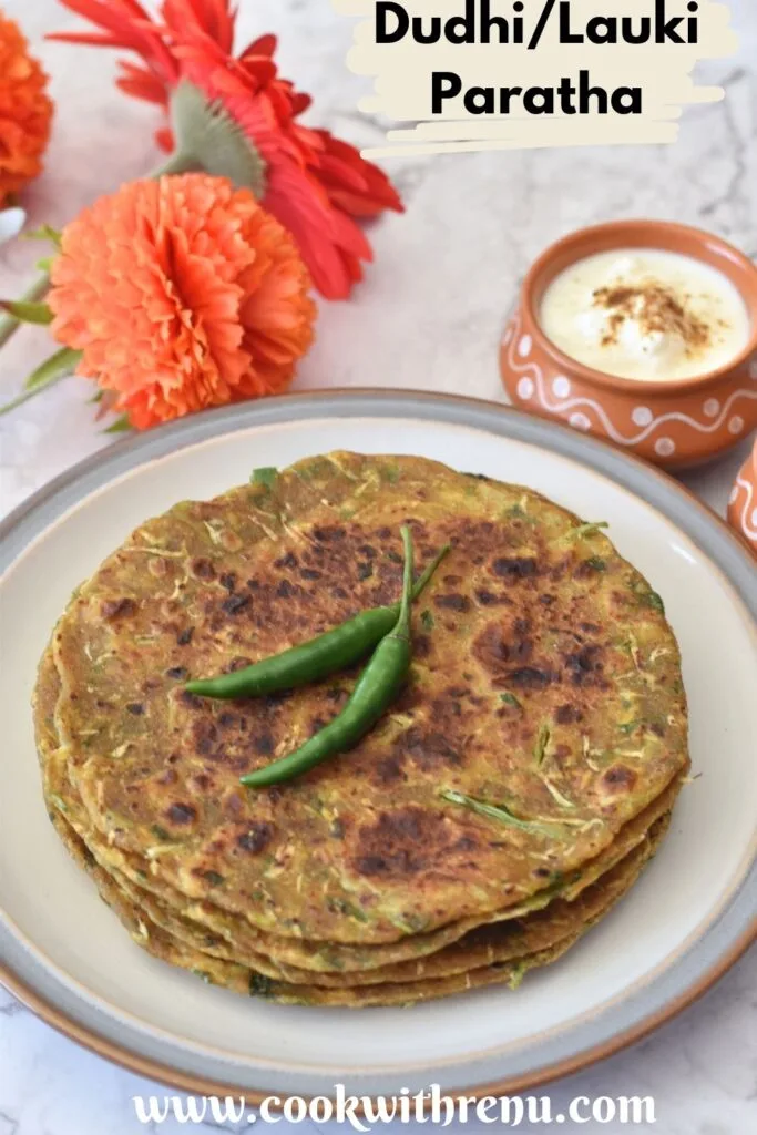3-4 Dudhi Paratha served in a white plate with some green chilies on top and some yogurt in a bowl.