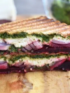 Close up look of Carrot Greens Pesto Beetroot Paneer Sandwich, which is cut open. Seen are the layers of pesto, paneer, onion and beetroot.