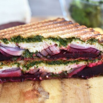 Close up look of Carrot Greens Pesto Beetroot Paneer Sandwich, which is cut open. Seen are the layers of pesto, paneer, onion and beetroot.