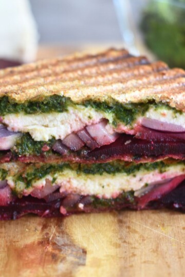 Close up look of Carrot Greens Pesto Beetroot Paneer Sandwich, which is cut open. Seen are the layers of pesto, paneer, onion and beetroot.