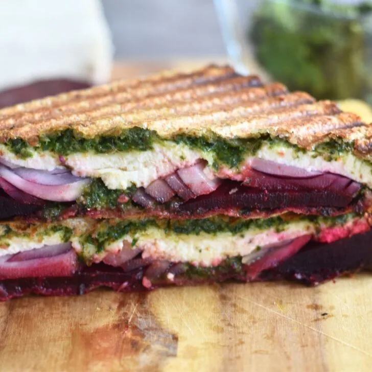 Close up look of Carrot Greens Pesto Beetroot Paneer Sandwich, which is cut open. Seen are the layers of pesto, paneer, onion and beetroot.