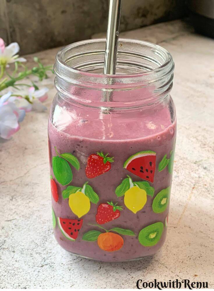 Banana Berry Protein Smoothie served in a glass with a steel straw in it. Seen in the background are some flowers.