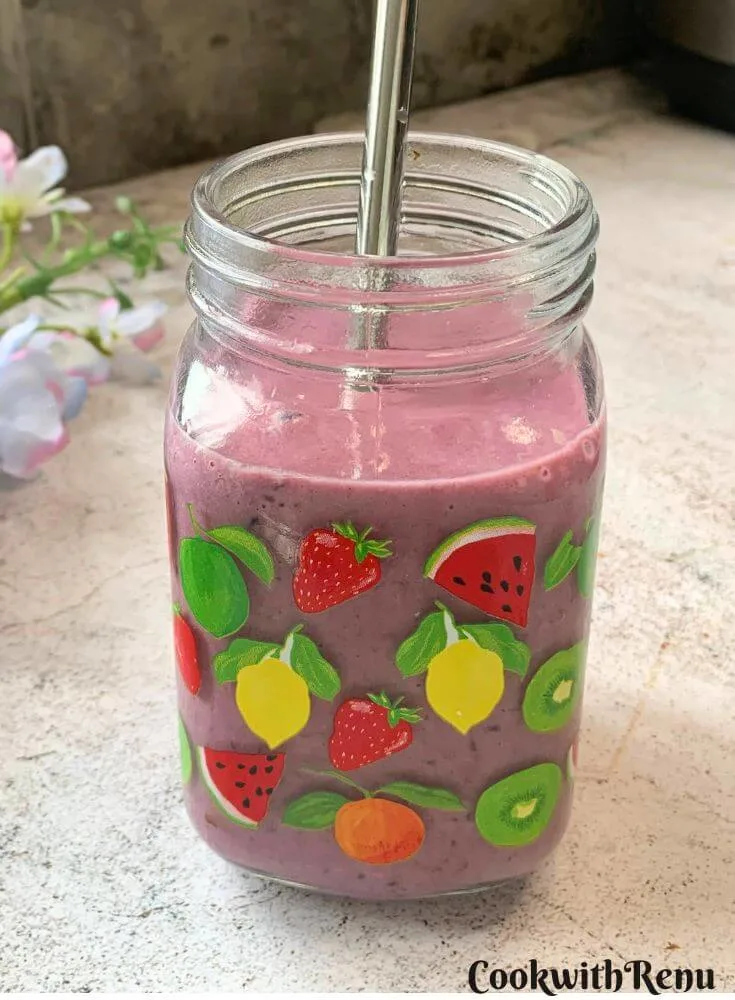 Banana Berry Protein Smoothie served in a glass with a steel straw in it. Seen in the background are some flowers.