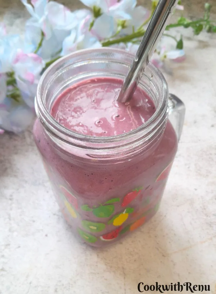 Banana Berry Protein Smoothie served in a glass with a steel straw in it. Seen in the background are some flowers.