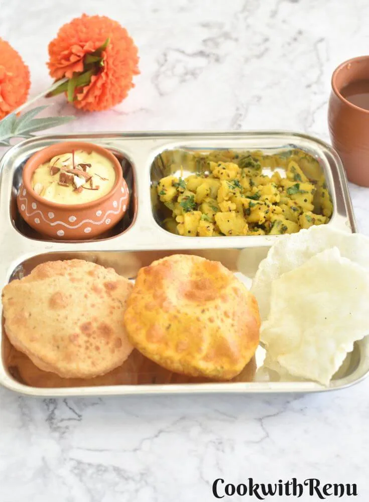 A steel divider plate, filled with 2 Puris, aloo bhaji and Shrikhand, and some papad.