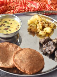 Thali featuring, Upaas ki thali with makhana kheer, aloo kali mirch, crispy kuttu pakoda, and puri, in clockwise directrion starting from top. A glass of water is on the side.