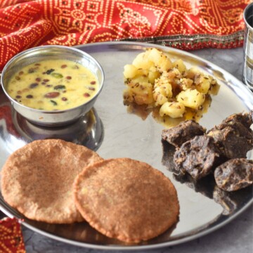 Thali featuring, Upaas ki thali with makhana kheer, aloo kali mirch, crispy kuttu pakoda, and puri, in clockwise directrion starting from top. A glass of water is on the side.