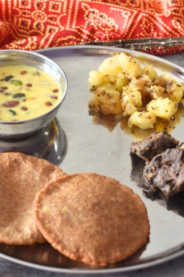 Thali featuring, Upaas ki thali with makhana kheer, aloo kali mirch, crispy kuttu pakoda, and puri, in clockwise directrion starting from top. A glass of water is on the side.