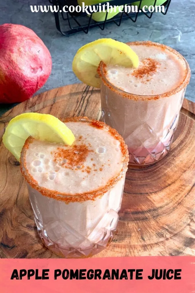 Apple Pomegranate Juice served in 2 glasses with a garnish of lemon and some salt, and spice mix. Seen in the background are some fruits.