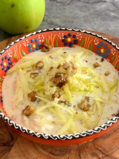Green Apple Walnut Raita served in an orange designer bowl. Seen in the background are some crisp green apples and a tree.
