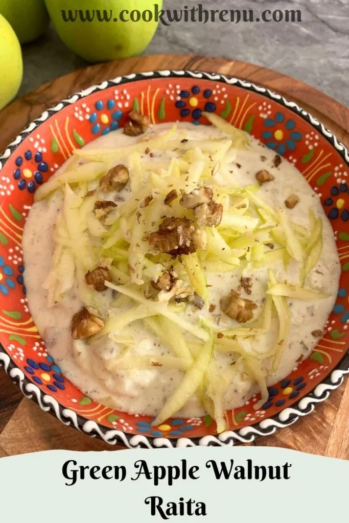 Green Apple Walnut Raita served in an orange designer bowl. Seen in the background are some crisp green apples and a tree.