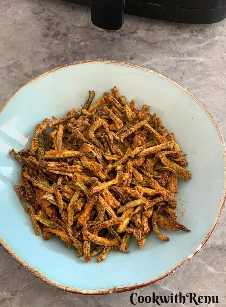 Air Fryer Kurkuri Bhindi in a light blue bowl. Seen in the background is the air-fryer. 