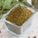 Mint Podi in a rectangular glass bowl. Seen in the background is some mint leaves.