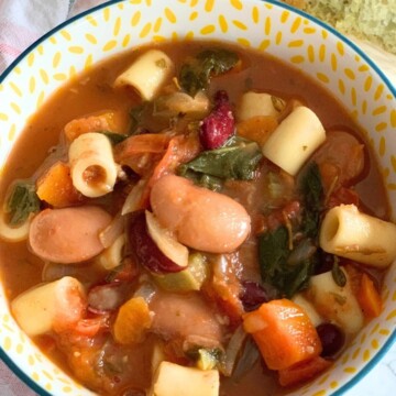 Close-up look of Minestrone Soup served in a bowl, seen in the background, is some chutney-spiced focaccia.