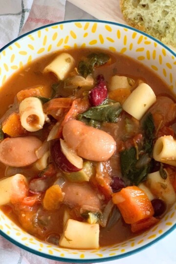 Close-up look of Minestrone Soup served in a bowl, seen in the background, is some chutney-spiced focaccia.